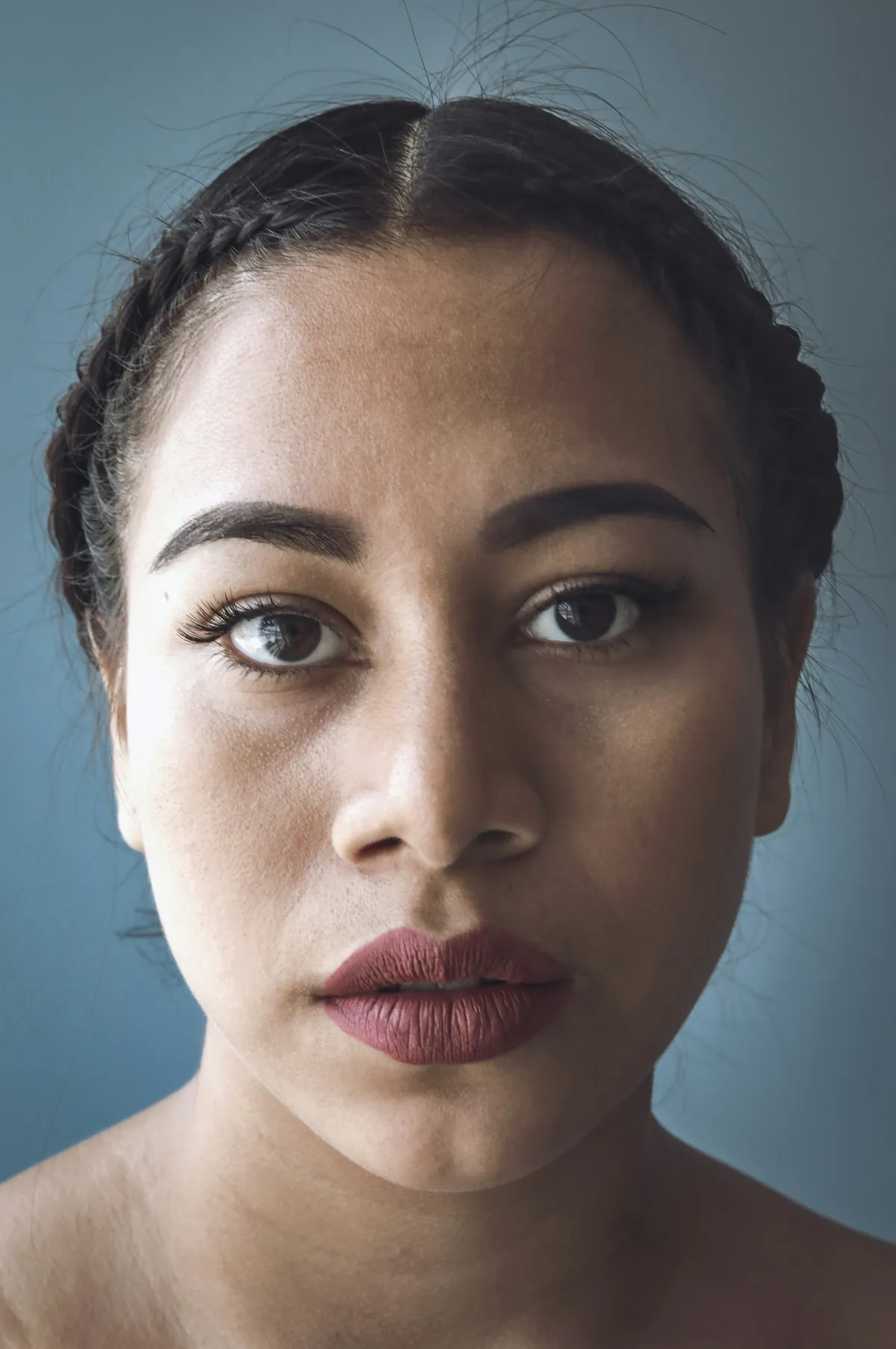 Close-up of a woman's face with braided hair against a blue-grey background