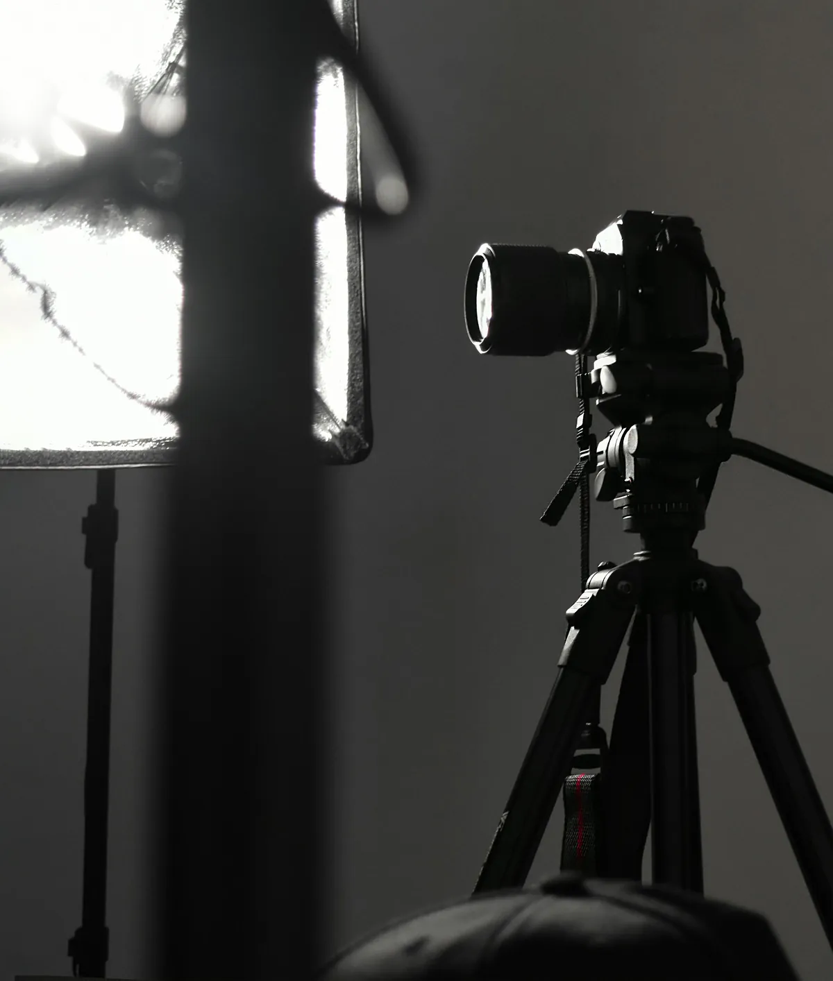 Camera on a tripod next to a studio light, black and white